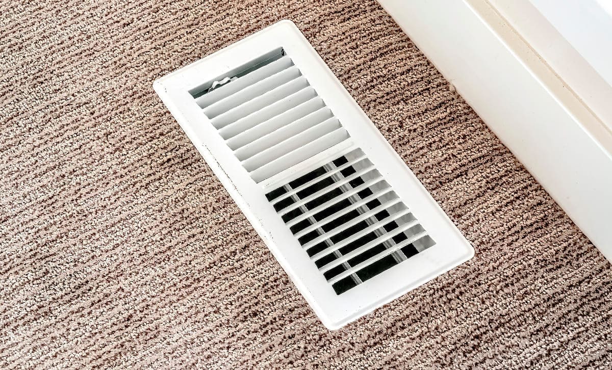 White air conditioner duct grille cover against floor with brown carpet